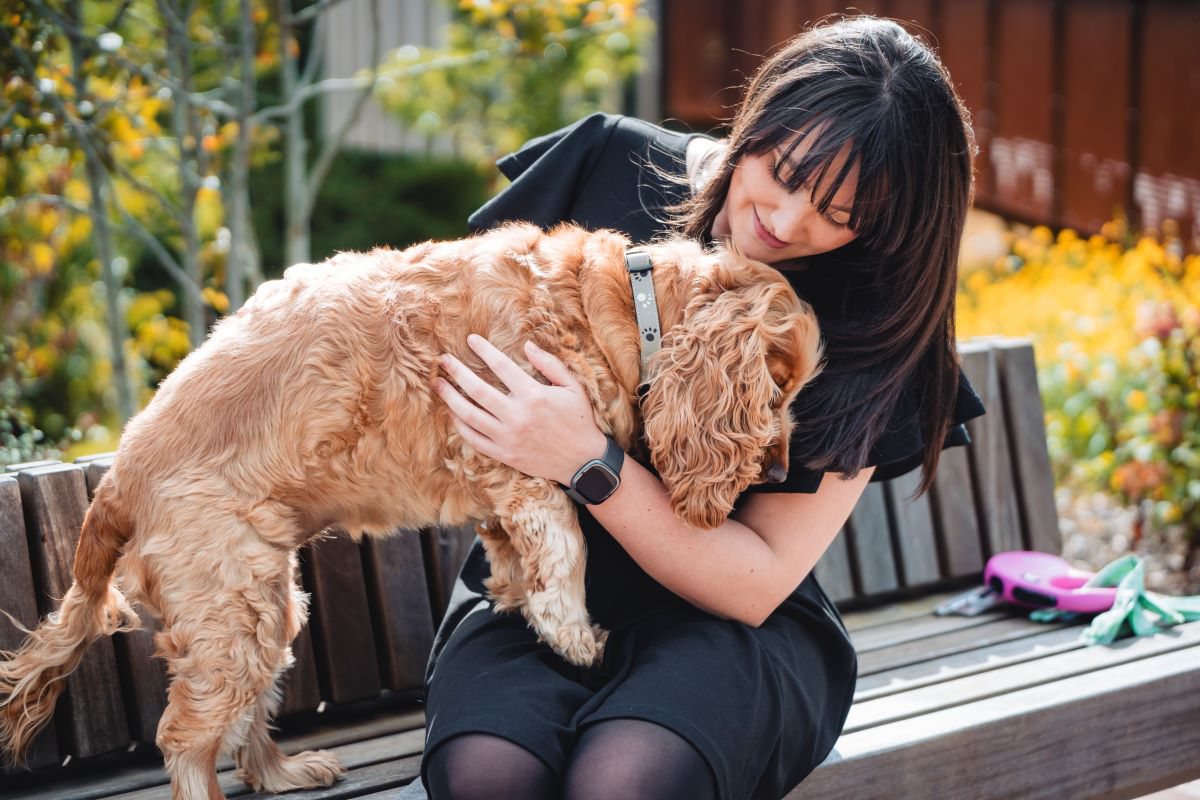 Woman smiling at a dog in a grassy field.