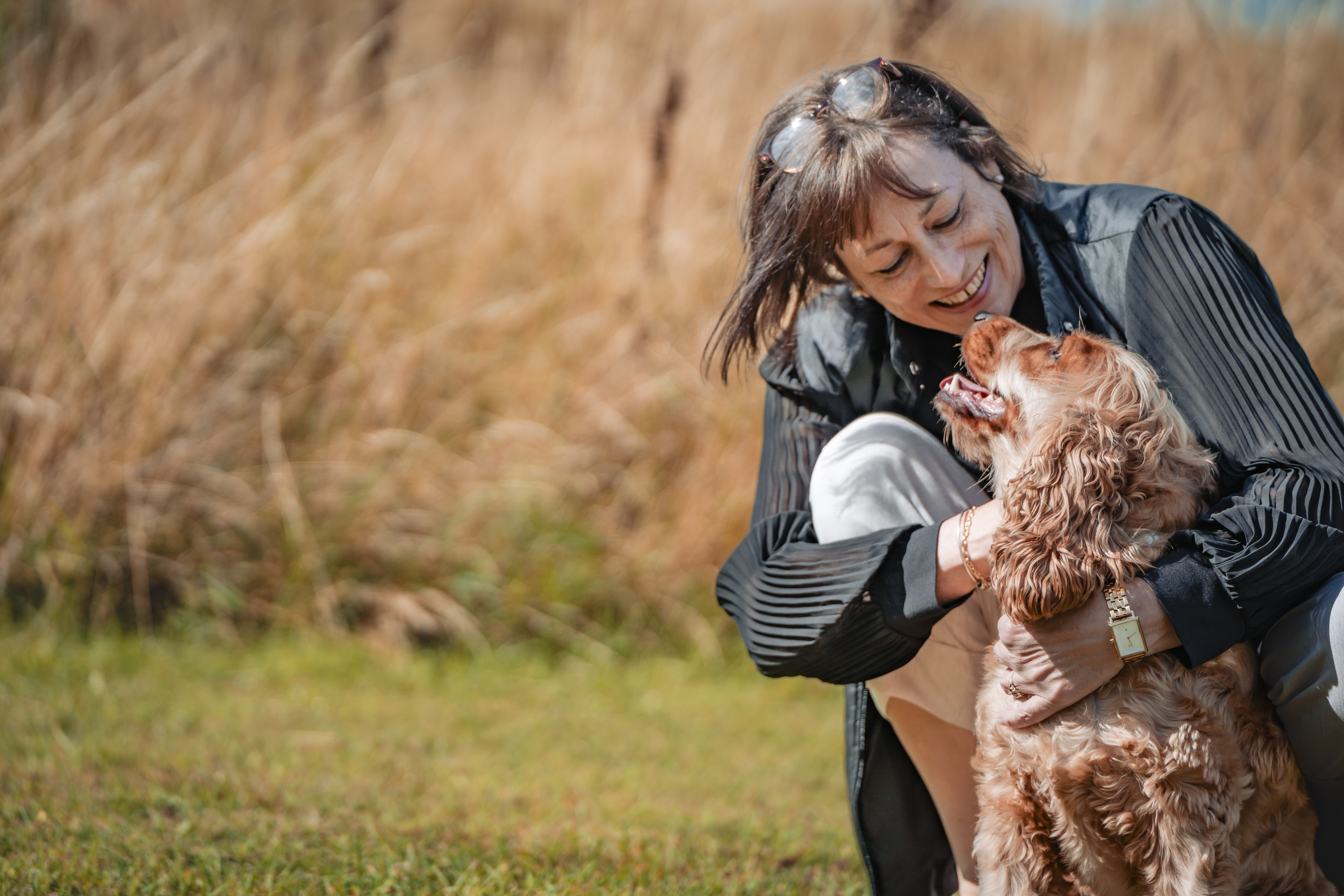 Woman smiling and hugging a dog in a grassy field.