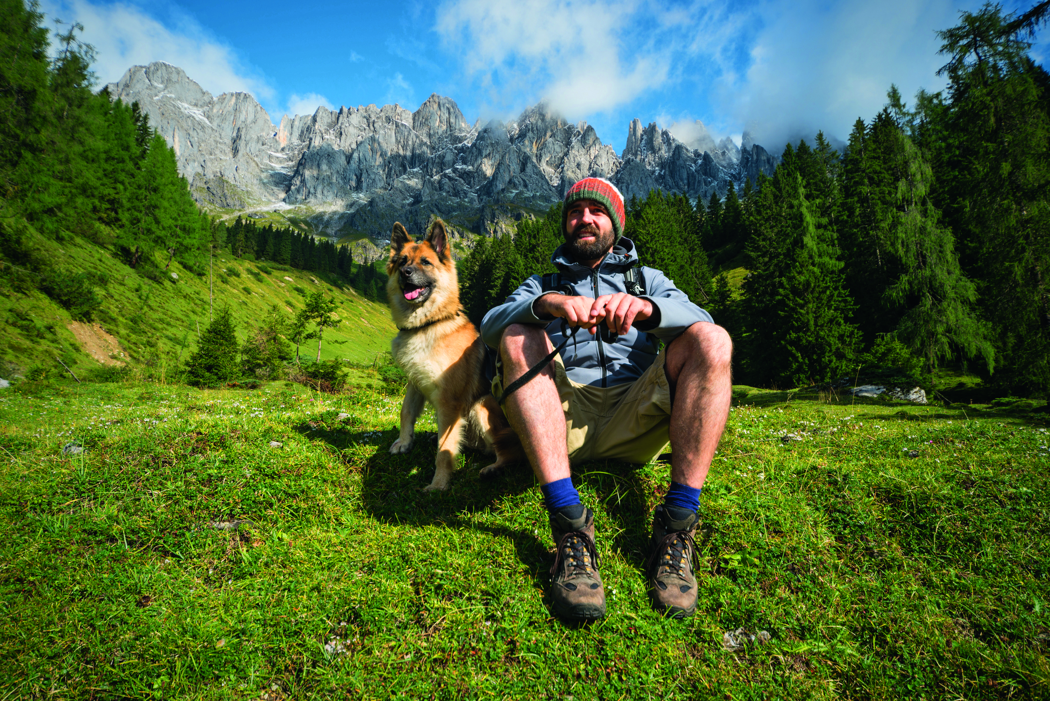 Ein Mann und sein Deutscher Schäferhund sitzen in einem friedlichen Bergwald.