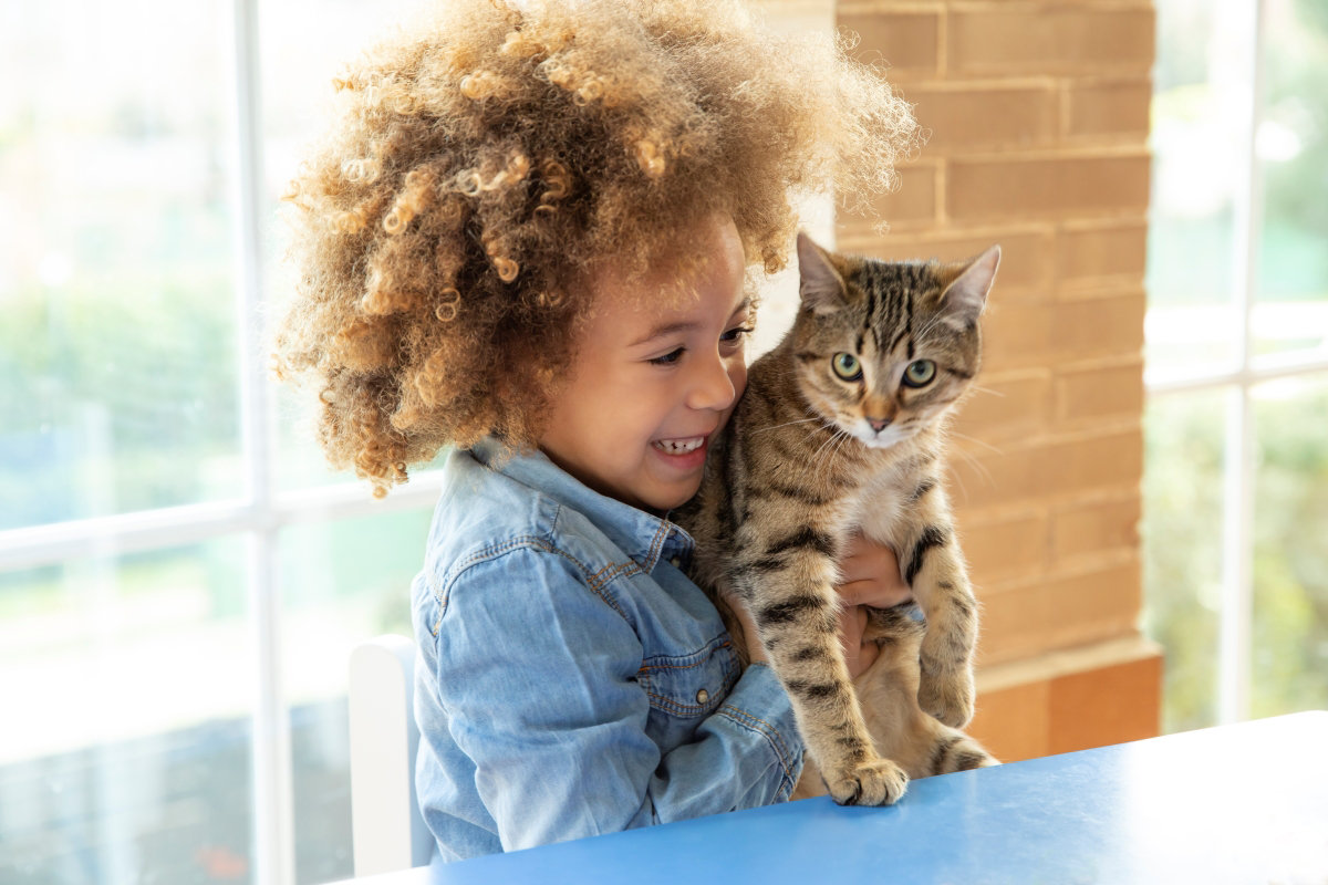 Child holding a tabby cat indoors with a smile.