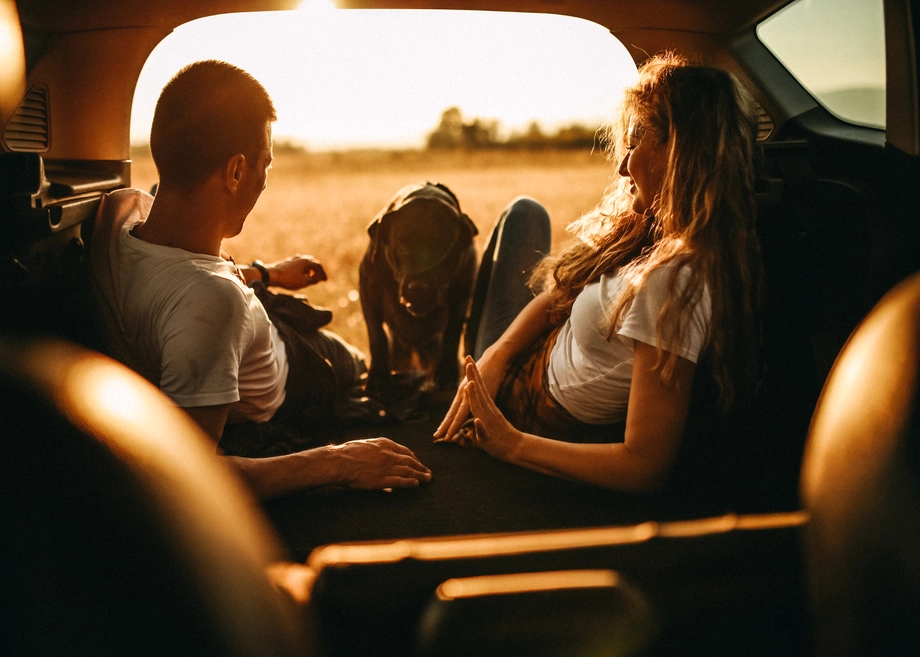 A couple and their dog relaxing in the back of a car at sunset.