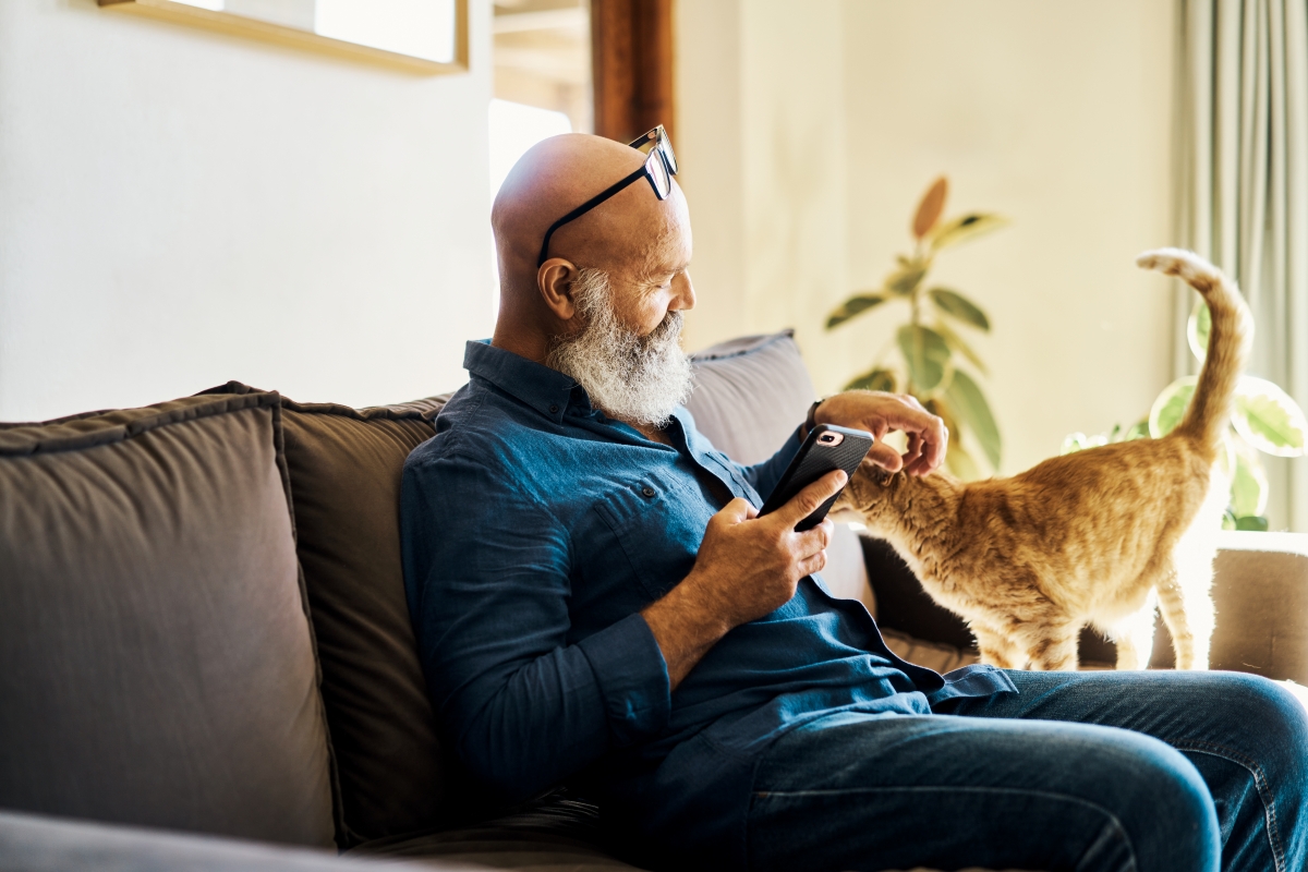Un hombre acariciando a un gato mientras sostiene un teléfono en un sofá.