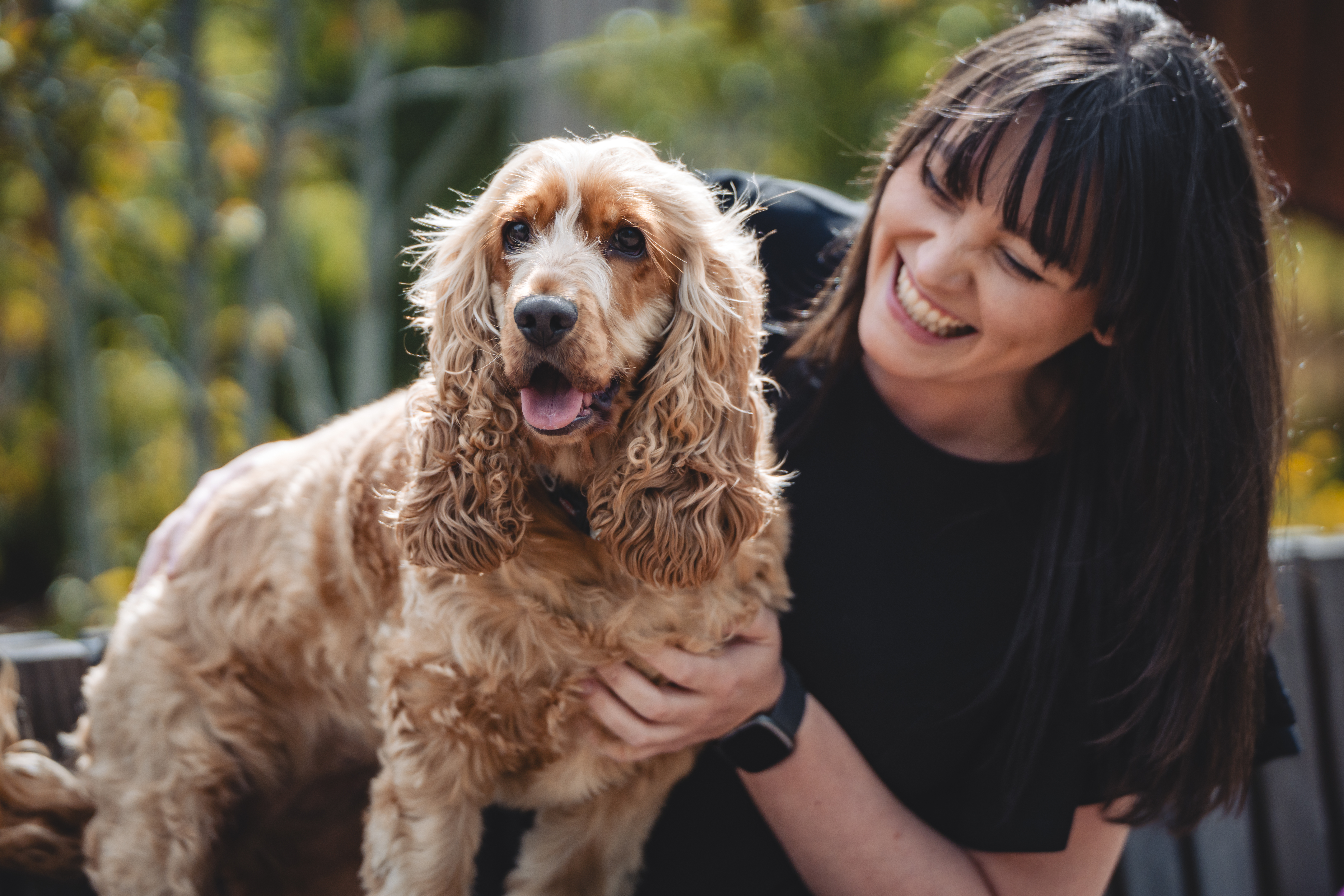 Smiling woman holding a happy spaniel dog outdoors.