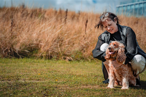 Woman kneeling in a field, smiling at a dog.