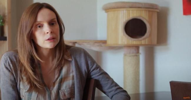 Una mujer sentada en el interior, cerca de un árbol para gatos.